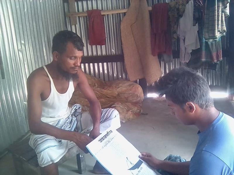 মাছের গদিতে জেলে মো. ইউসুফ হাওলাদারকে পত্রিকা পড়ে শোনাচ্ছে তারই সহযোগী মো. সোহাগ
