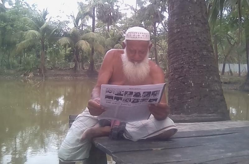 ভর দুপুরে গাছের ছায়ায় বসে আন্ধারমানিক কমিউনিটি পত্রিকায় চোখ বুলাচ্ছেন গ্রামের প্রবীণ ব্যক্তি মো. সামসুদ্দিন নাজির